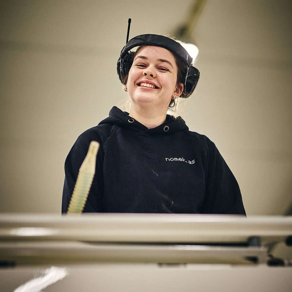 Smilende ansatt med hodetelefoner på, fra Nomeks mekaniske verksted i Stryn