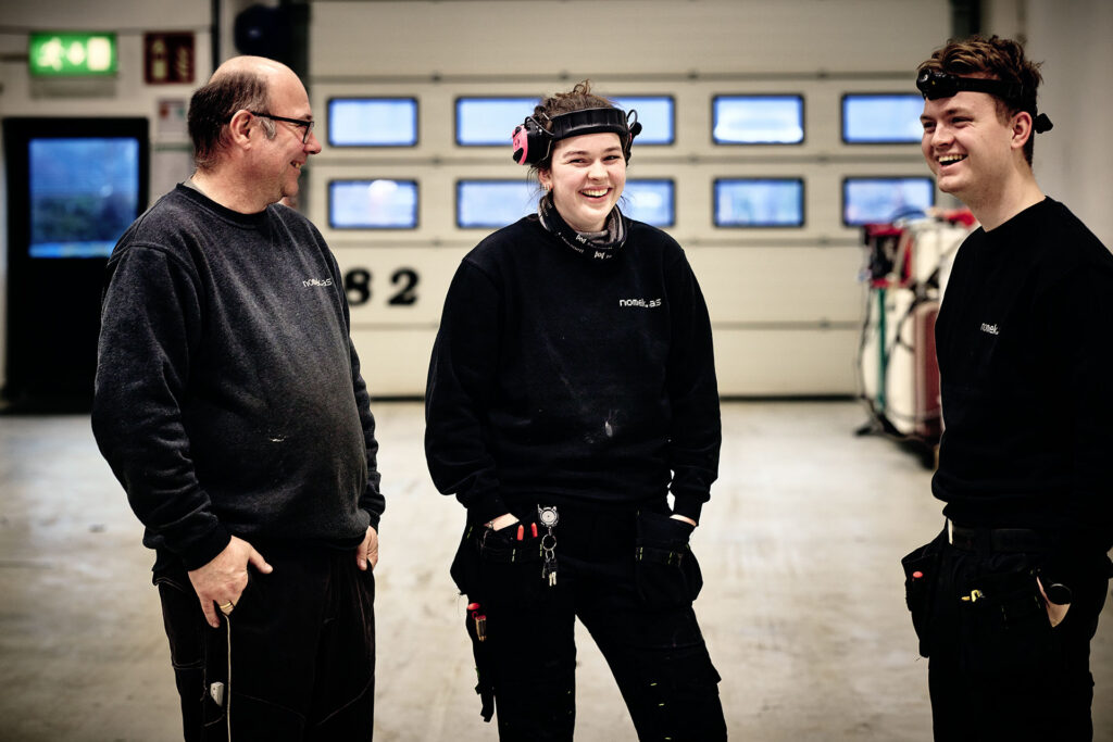 Tre smilende ansatte på jobb hos Nomek, her på Nomek sitt verksted i Stryn