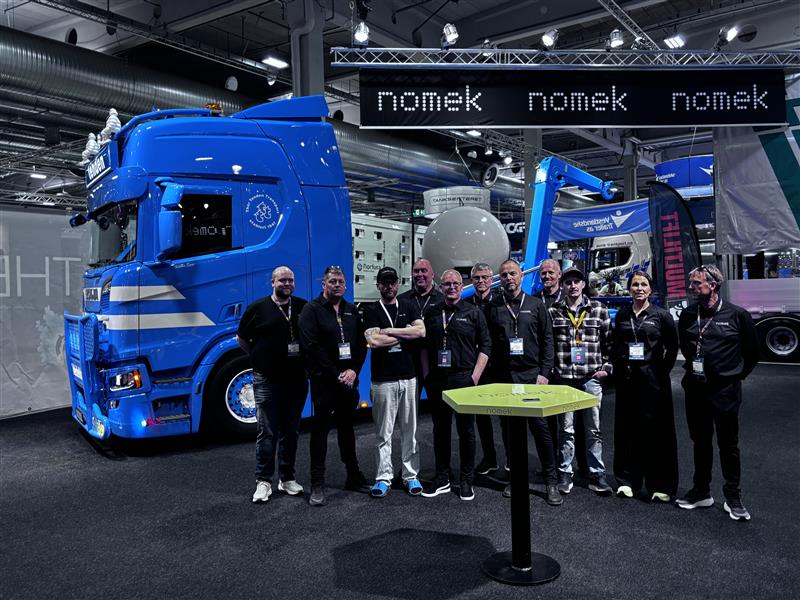 Ansatte fra Nomek samlet foran en blå lastebil med krokpåbygg på Transport 2026-messen.